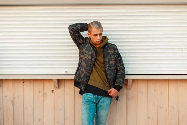 Stijlvol trendy man in een trendy militaire jas en een hoodie met jeans poseren op strand — Stockfoto