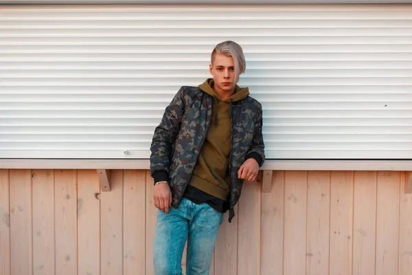 Stijlvolle knappe man in een militaire jas en jeans permanent in de buurt van de muur — Stockfoto