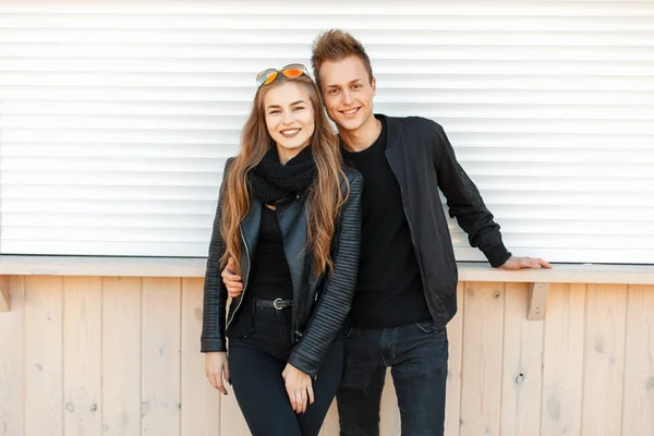 Красива щаслива молода пара посміхається в стильному модному одязі біля білої стіни — стокове фото