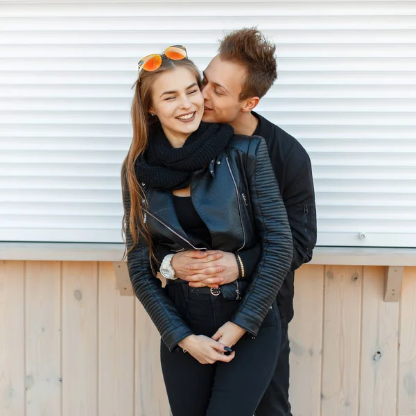 Красива щаслива пара в модному осінньому одязі з сонцезахисними окулярами біля дерев'яної стіни — стокове фото