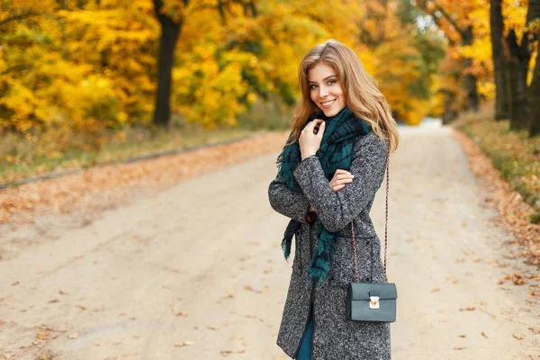 Mujer joven hermosa feliz en un abrigo de otoño con una bufanda sobre un fondo de follaje amarillo — Foto de Stock