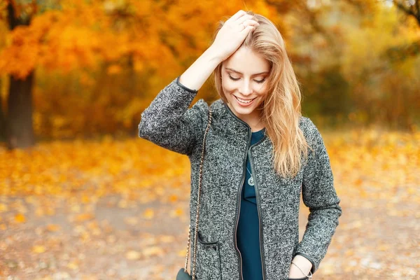 Красива молода щаслива жінка в модному осінньому одязі, що йде в парку з жовтим листям — стокове фото