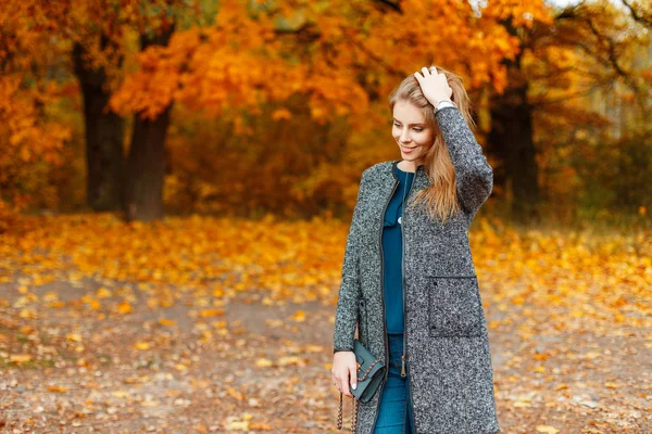 Glückliche junge Frau mit einem Lächeln in modischer Herbstkleidung, die neben Bäumen mit gelbem Laub posiert — Stockfoto