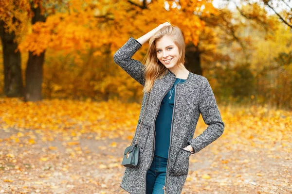 Mooie stijlvolle jongedame met een glimlach in herfst kleding in de buurt van bomen met gele bladeren — Stockfoto