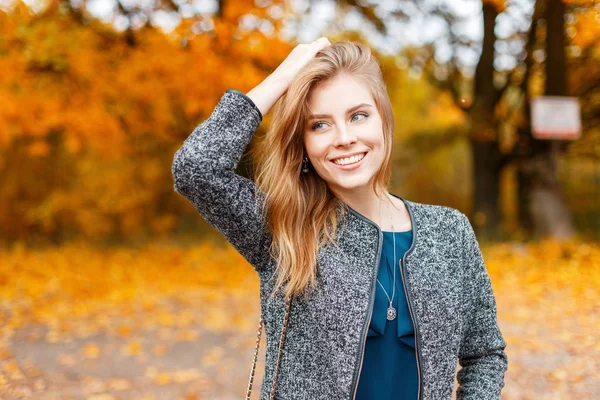 Glückliche schöne junge Frau mit einem Lächeln im Mantel im Herbsttag — Stockfoto