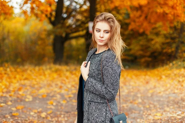 Happy beautiful young woman with a smile in a trendy coat posing in a yellow autumn park — Stock Photo, Image