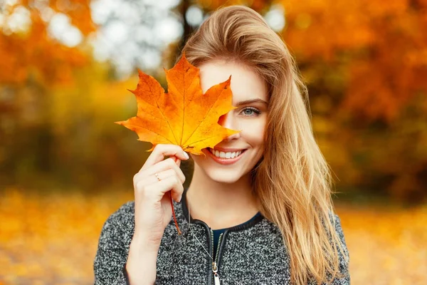 Beautiful happy woman with a smile holds an autumn yellow leaf near the face — Stock Photo, Image