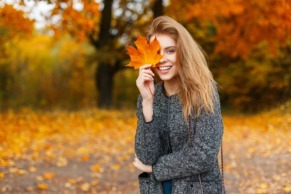 Happy young beautiful woman with a smile holds an autumn yellow leaf in the autumn day in the park — Stock Photo, Image