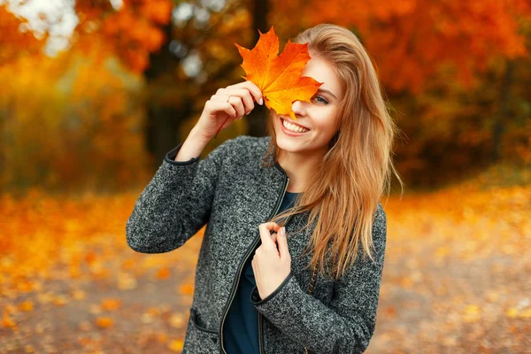 Hermosa mujer feliz con una hoja de color amarillo brillante en un parque de otoño — Foto de Stock