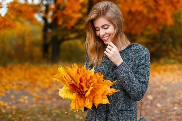 Красива щаслива дівчина з посмішкою тримає букет жовтого листя в осінньому парку — стокове фото