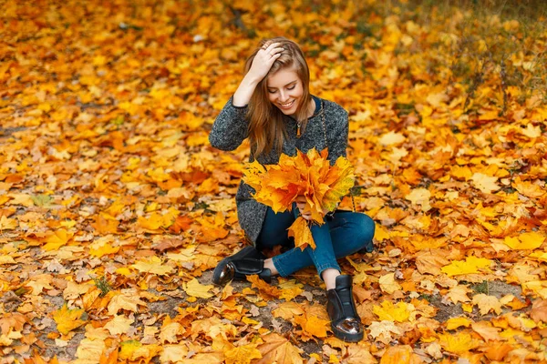 Grappige gelukkige vrouw met een glimlach houdt gele herfst bladeren en bevindt zich in gebladerte — Stockfoto
