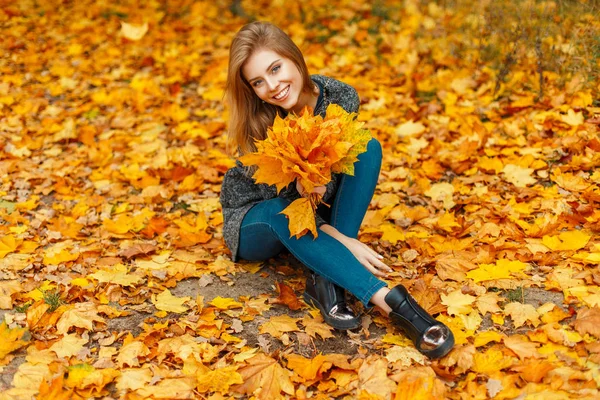 Schöne, fröhliche Frau mit einem Lächeln in fröhlicher Stimmung mit einem Strauß Blätter in einem herbstgelben Laub — Stockfoto