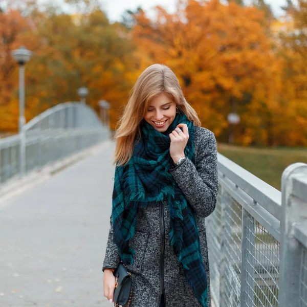 Mulher jovem no casaco elegante com passeios de lenço na moda no dia de outono contra um contexto da folhagem amarela — Fotografia de Stock