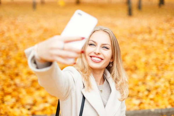 Menina feliz com um sorriso fazendo selfie em um dia de outono contra um fundo de folhagem amarela — Fotografia de Stock