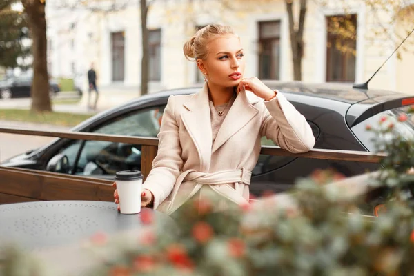 Beautiful young business woman in a classic coat with a cup of coffee resting on the street — Stock Photo, Image