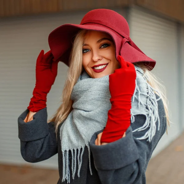 Porträt einer schönen glücklichen Frau mit einem Lächeln im modischen Hut und einem grauen Mantel mit grauem Schal im Freien — Stockfoto