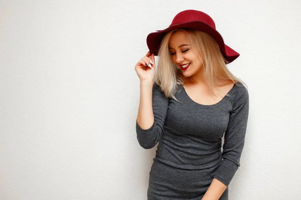 Piękny model młoda kobieta w modzie kapelusz w kolorze szarym sukienka uśmiechający się w pobliżu białej ścianie — Zdjęcie stockowe