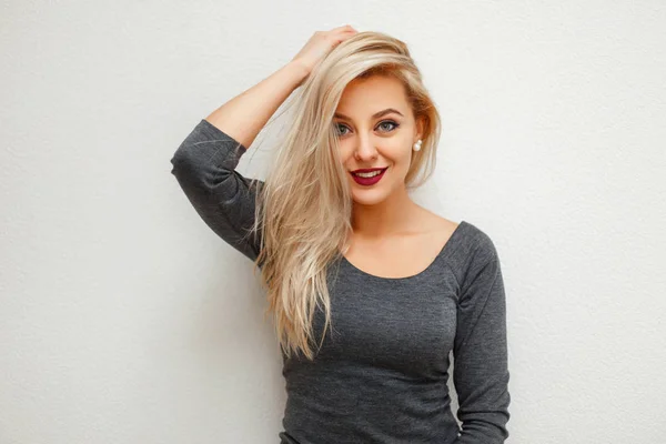 Hermosa mujer rubia de moda en un vestido gris posando cerca de una pared blanca —  Fotos de Stock