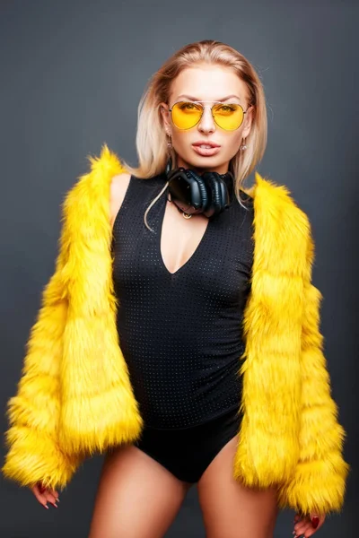 Chica joven con estilo de moda con gafas de sol amarillas de verano y un abrigo de piel amarillo de moda sobre un fondo gris —  Fotos de Stock