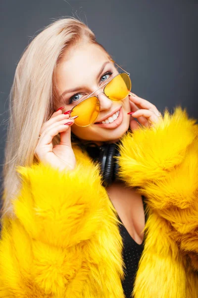 Retrato de una hermosa joven con auriculares en gafas de sol de moda amarilla con un abrigo de moda amarillo sobre un fondo gris — Foto de Stock