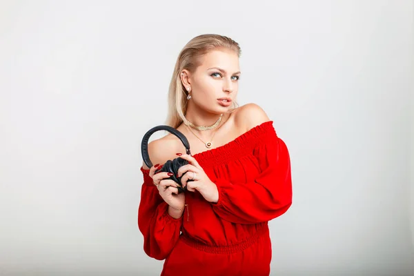 Schöne junge Model-Mädchen mit Kopfhörern in einem stilvollen roten Kleid auf grauem Hintergrund — Stockfoto