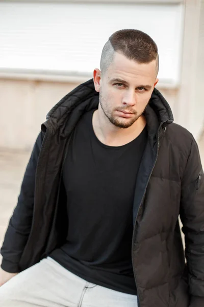 Joven hombre guapo con un peinado corto en una chaqueta de invierno negro con estilo en la calle — Foto de Stock