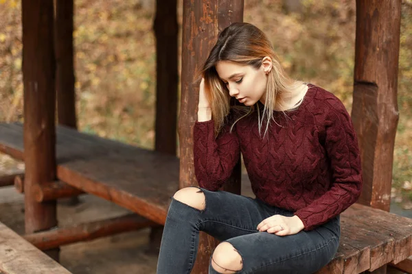 Schöne junge Frau im stylischen Strickpullover sitzt auf einer Holzbank in der Natur — Stockfoto