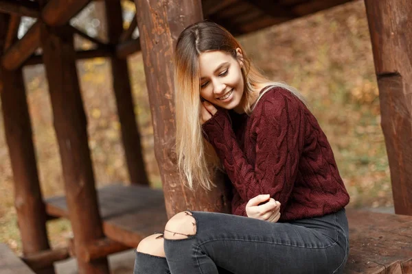 Glückliches junges Mädchen in stylischem Pullover sitzt in einer hölzernen Pergola. Natur Herbstmode — Stockfoto