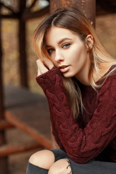 Mode Porträtt av en vacker ung blond flicka i en snygg tröja utomhus på hösten dagen sitter nära trä lodge — Stockfoto