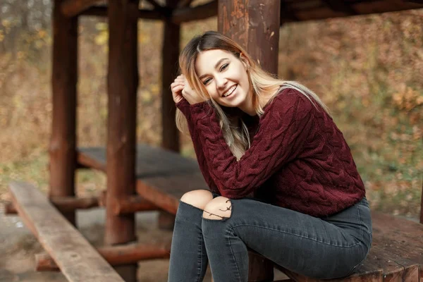 Szczęśliwy piękna młoda kobieta z uśmiechem w vintage sweter sweter siedzi w drewniane zadaszenie na zewnątrz w jesienny dzień — Zdjęcie stockowe