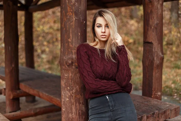 Stijlvolle jongedame in een trendy vintage trui vormt in de buurt van houten pilaren in de herfst dag — Stockfoto