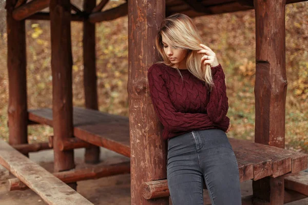 Stilvolle schöne Frau in einem modischen Pullover mit Jeans posiert in der Nähe eines hölzernen Pavillon — Stockfoto
