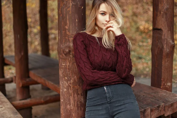 Menina loira jovem bonita em camisola de malha elegante e jeans perto de pilares de madeira — Fotografia de Stock