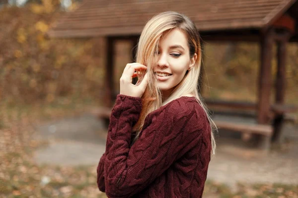 Feliz joven hermosa chica con una sonrisa en un suéter vintage de punto en la naturaleza cerca de una casa de madera favorecedora —  Fotos de Stock