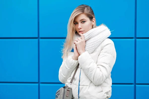 美丽的年轻女子与时尚针织围巾和白色冬季夹克与一个袋子在蓝色墙壁附近在冬天天 — 图库照片