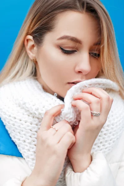 Stylish beautiful young woman with fashionable white knitted scarf and white winter jacket on a winter day. — Stock Photo, Image