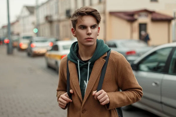 Joven viajero guapo en un abrigo vintage con estilo con una bolsa de viaje en la ciudad — Foto de Stock