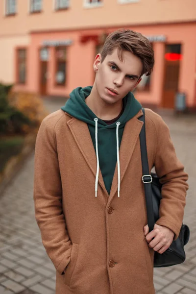 Модний молодий чоловік у стильному вінтажному пальто з мішком позує в місті — стокове фото