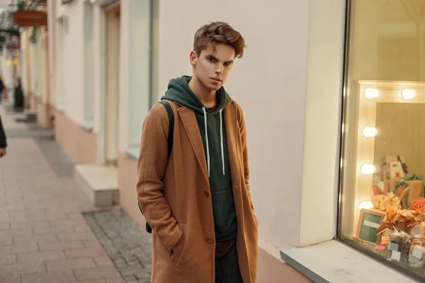 Stijlvolle jongeman met een kapsel in een trendy vintage jas in de buurt van de etalage — Stockfoto