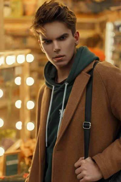 Joven de moda con un corte de pelo en un abrigo de moda vintage con una bolsa cerca de la tienda con bombillas — Foto de Stock