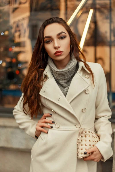 Mulher elegante na moda em um casaco da moda com uma bolsa elegante posando na rua — Fotografia de Stock