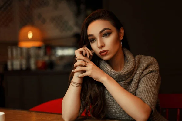 Piękna młoda kobieta marzyciel w stylowy sweter siedzi w kawiarni — Zdjęcie stockowe