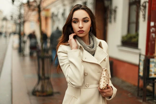 Mujer joven con estilo de moda en un abrigo de otoño de moda con una bolsa de moda caminando al aire libre en la ciudad — Foto de Stock