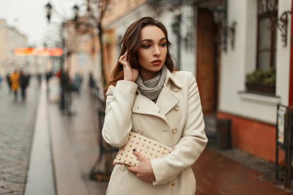 Модна красива молода жінка в стильному пальто з модним мішком, що йде на відкритому повітрі в місті — стокове фото