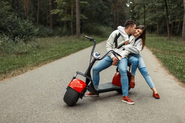 Jovem casal bonito elegante em roupas de marca na moda perto de bicicleta elétrica vermelha — Fotografia de Stock