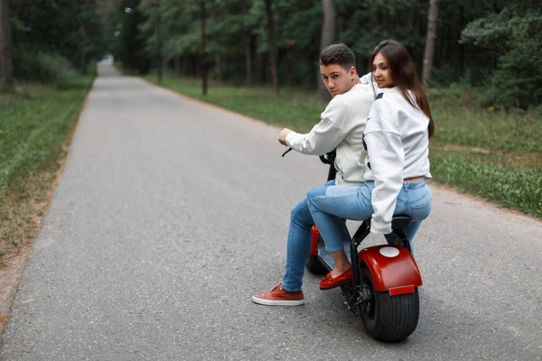 Hermosa pareja joven en pantalones vaqueros azules y suéteres blancos montar una bicicleta electrónica — Foto de Stock