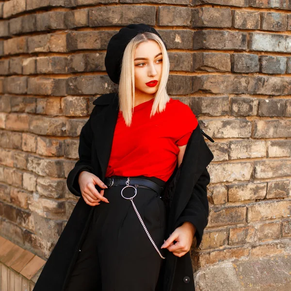 Mulher elegante bonita em um casaco preto na moda perto de uma parede de tijolo — Fotografia de Stock