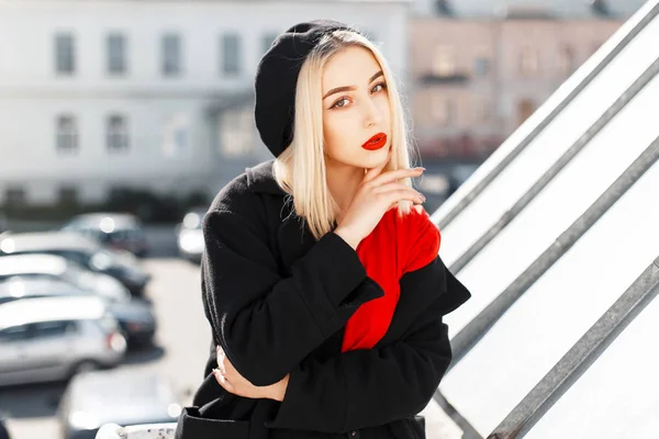 Ritratto di una bella giovane donna bionda con labbra rosse in cappotto nero e basco all'aperto in una giornata autunnale soleggiata — Foto Stock