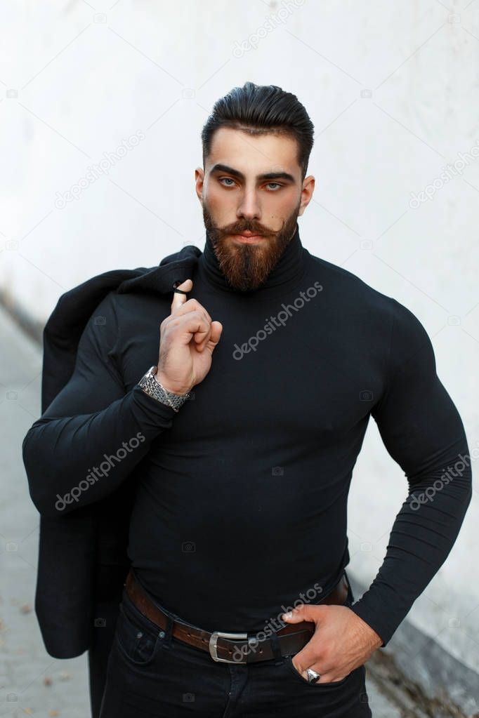Strong handsome man in a black coat in a black shirt with the beard and mustache posing on the street