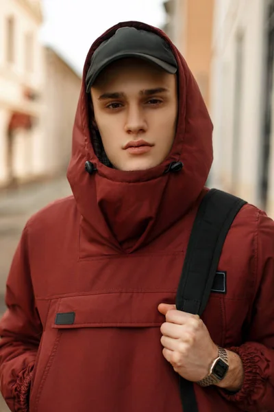 Handsome young guy in a sporty red jacket with a hat and a black — Stock Photo, Image